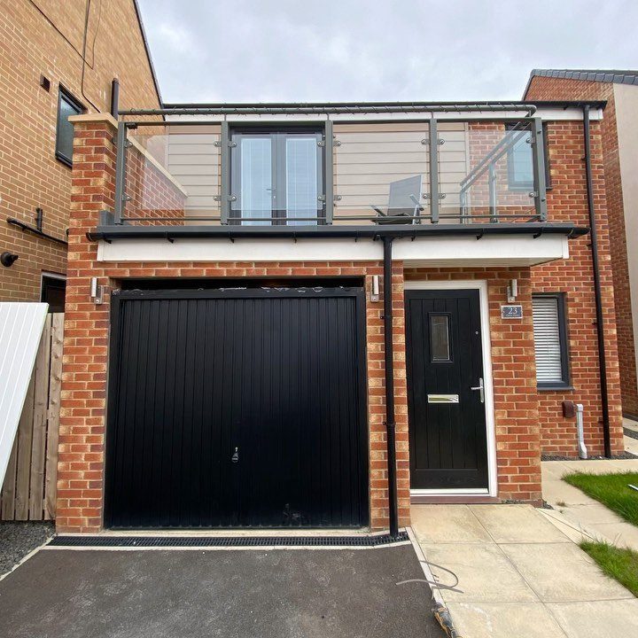 Red brick house with a black garage door and an upper balcony with glass railings.