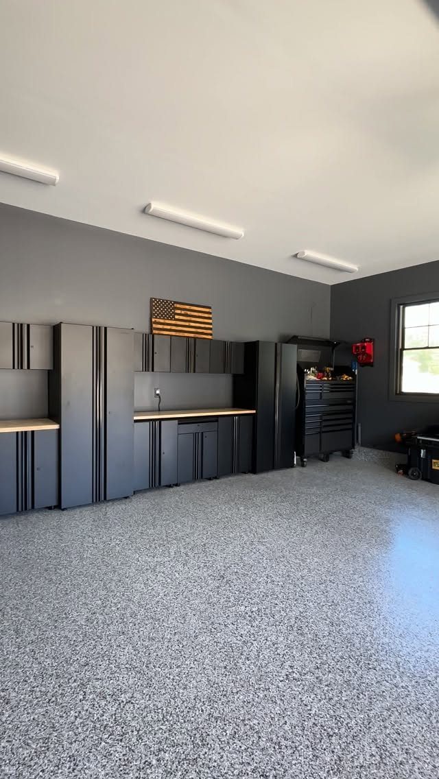 Dark grey garage walls with black cabinets and a speckled grey epoxy floor.