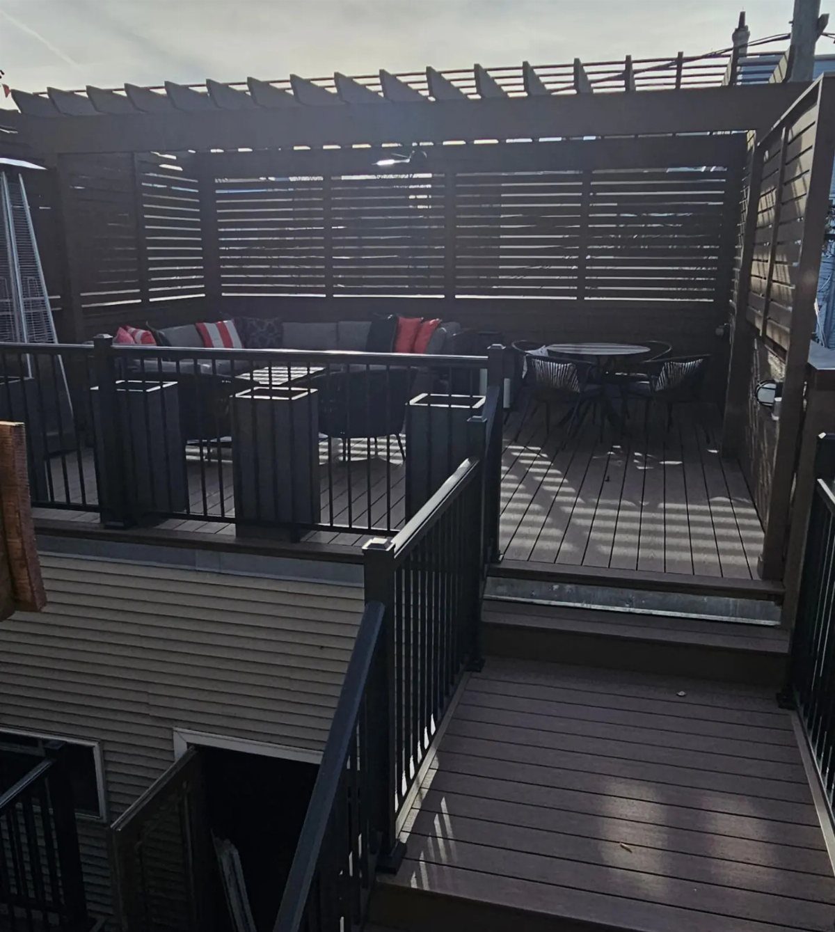Garage Rooftop Deck: 8 Ideas for Your Space Above 5 A dark wood rooftop deck with a pergola, lounge seating, and a dining area under a clear sky.