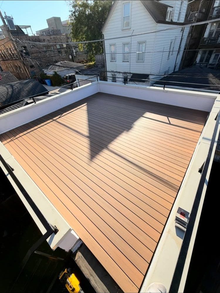 Garage Rooftop Deck: 8 Ideas for Your Space Above 8 A wooden plank rooftop deck enclosed by a white wall and black metal railing in an urban setting.