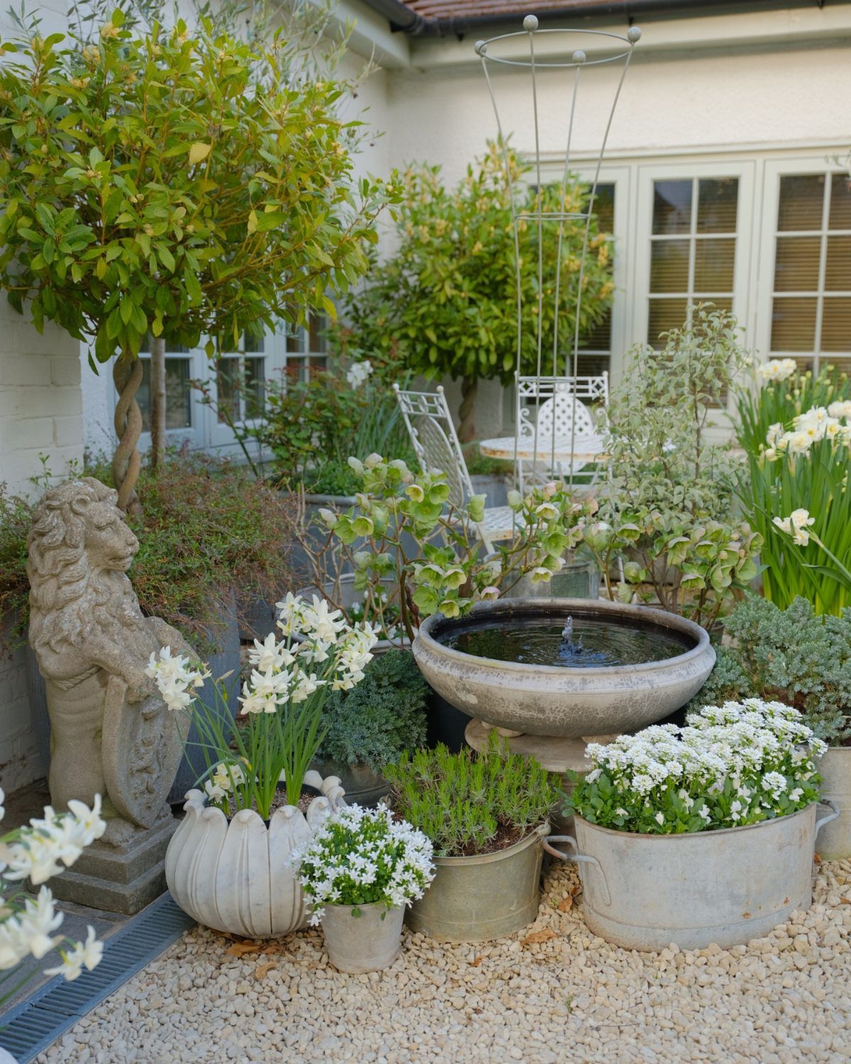10 Garden Front of House Ideas: From Foundation Beds to Arbors 2 Potted plants with white flowers arranged in various containers on a gravel garden patio.