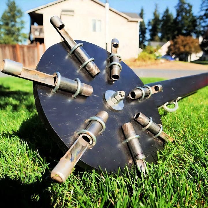 A metal circular lawn aerator tool with multiple tines resting on green grass.