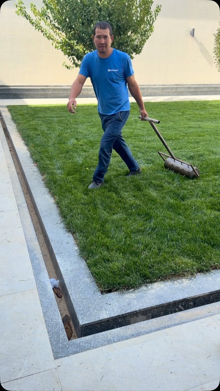 A man pulling a homemade cylindrical lawn aerator tool across a green grass lawn.