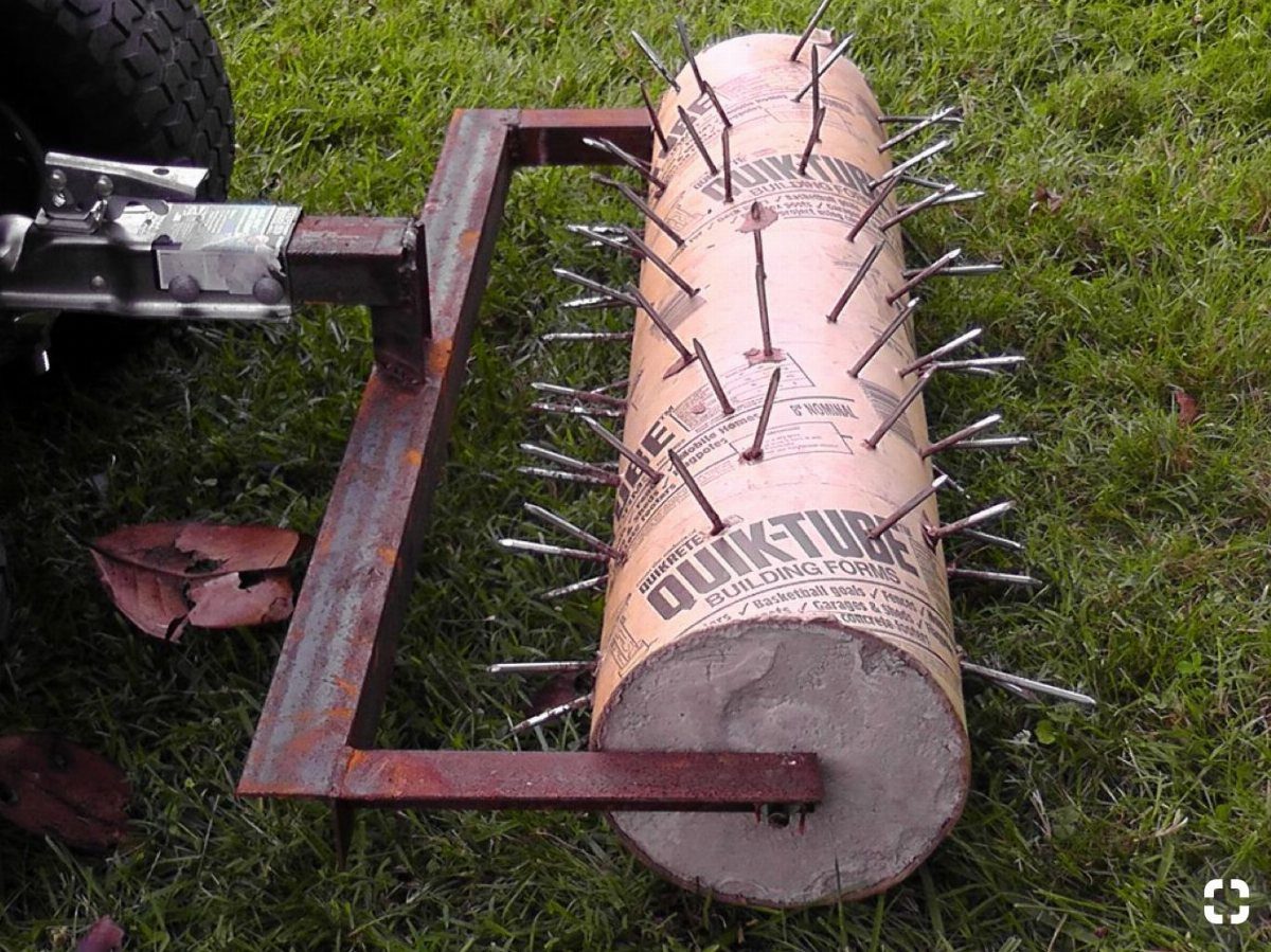 A homemade lawn aerator made of concrete and nails resting on green grass.