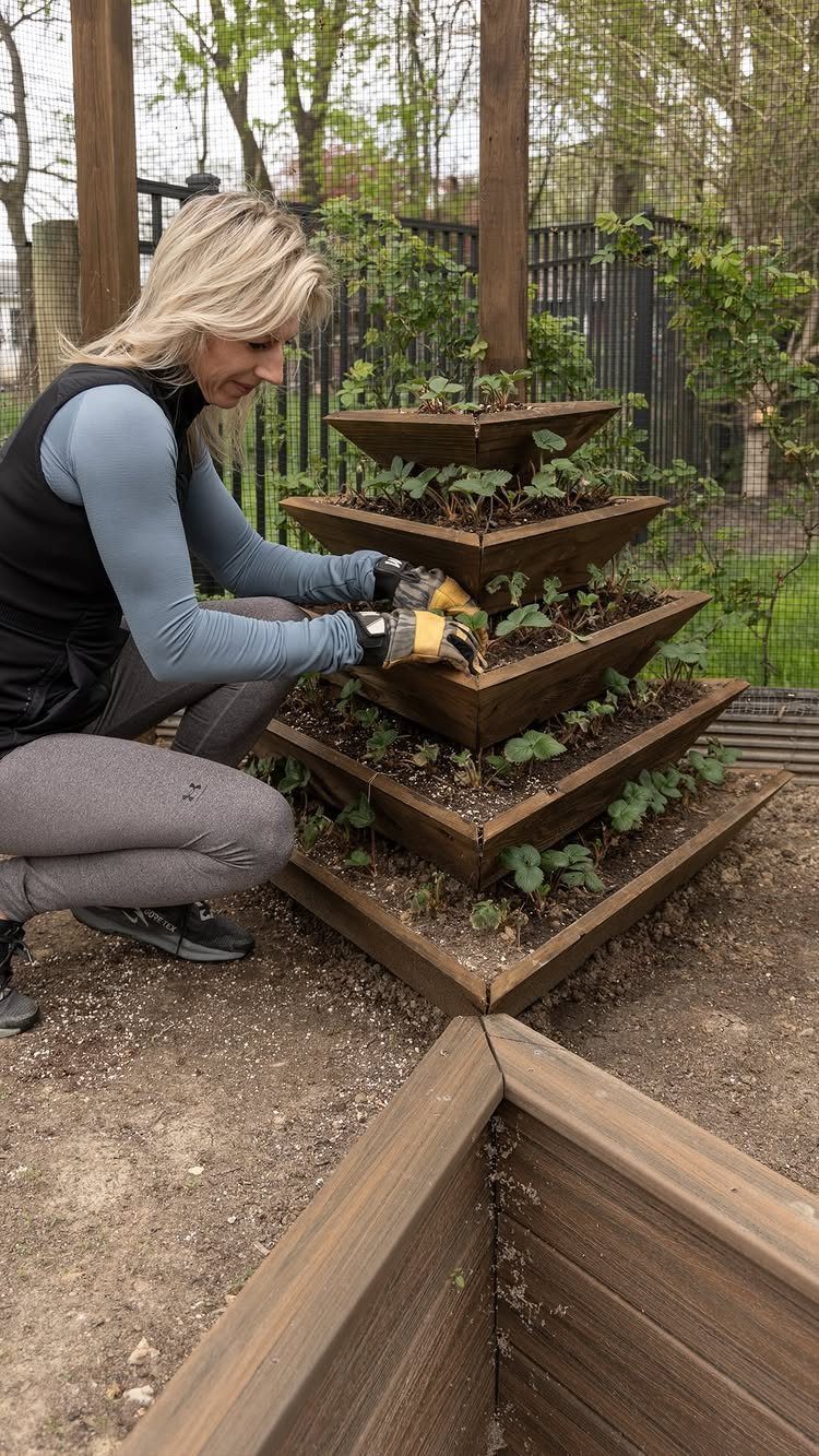 A woman tending to green plants in a tiered wooden pyramid planter in a garden.