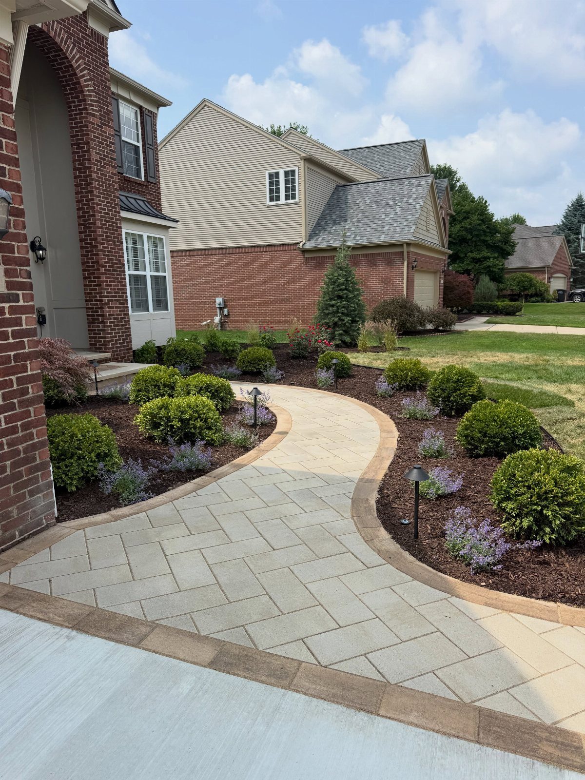 11 Landscaping Front Walkway Ideas: Flagstone to Paver & Modern Styles 4 A curved paver walkway with herringbone pattern and tan edging winding through a landscaped garden bed.