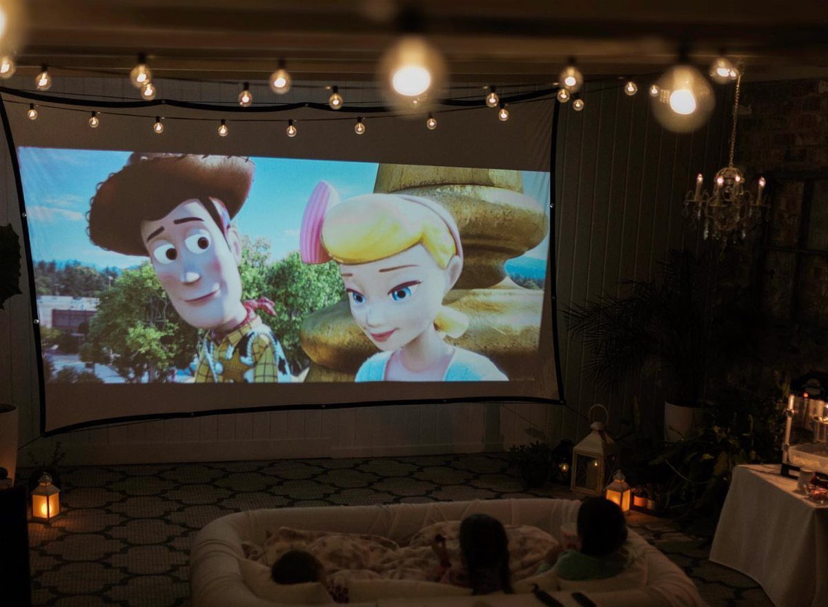 16 Low Budget Backyard Ideas to Refresh Your Outdoor Space 12 Animated characters on a large outdoor projector screen with people lounging on a beanbag below.