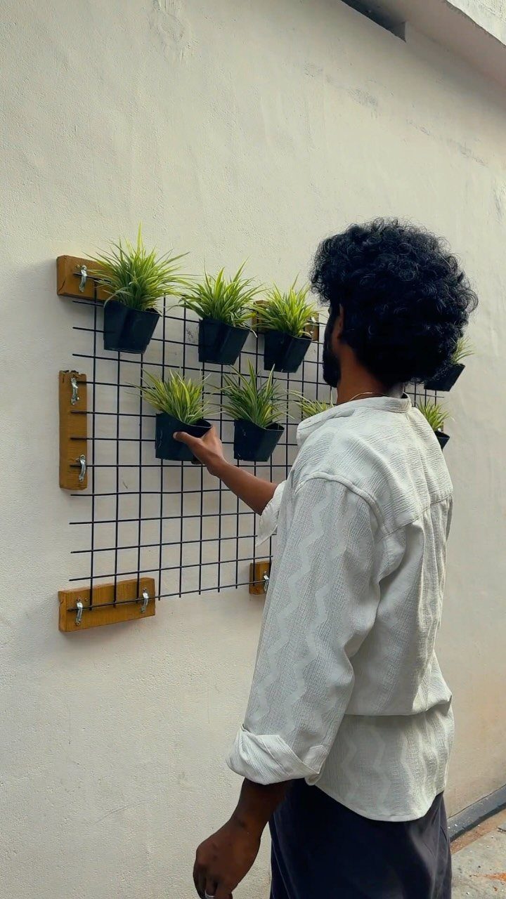 16 Low Budget Backyard Ideas to Refresh Your Outdoor Space 15 A man arranging small potted plants on a black wire grid mounted to a white wall.