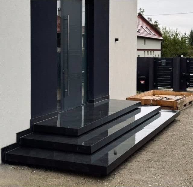 Black polished stone steps leading to a modern dark glass front door of a white house.