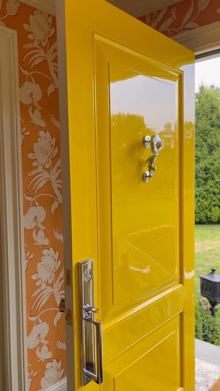 A bright yellow glossy front door stands open against orange floral wallpaper.