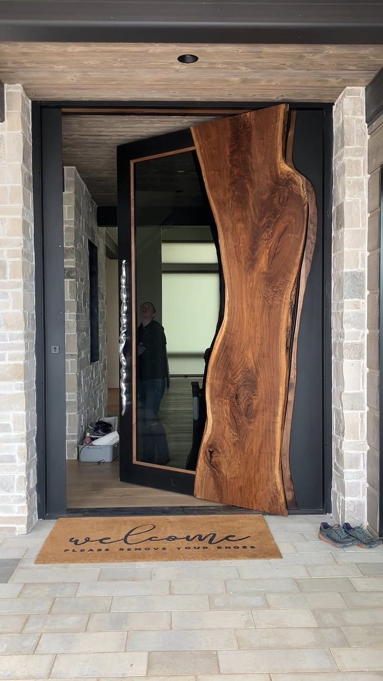 A modern front door featuring a large, natural live-edge wood slab and dark metal frame.