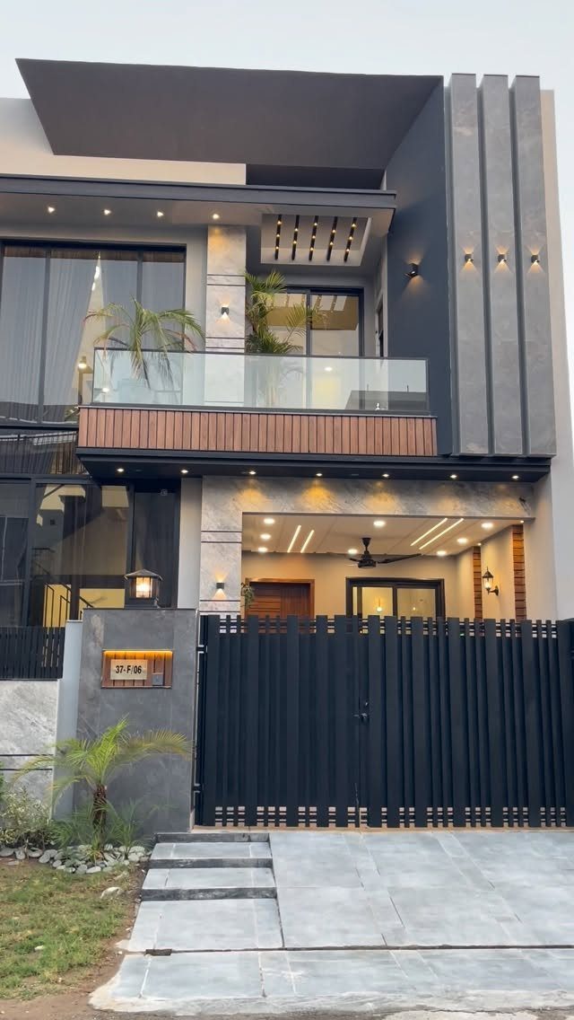 Modern two-story house with dark grey walls, glass balcony, and a black metal gate.