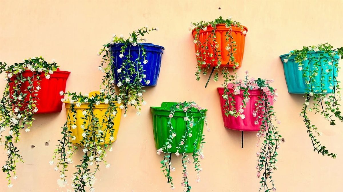 9 Outdoor Flower Pots Ideas with Window Boxes, Trellises & Wall Pots 7 Colorful plastic pots with trailing green plants and white flowers mounted on a peach wall.