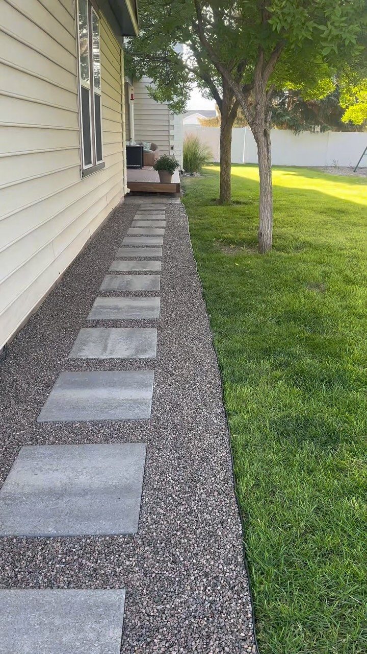 Grey rectangular stone pavers set into a narrow gravel path alongside a house and lawn.