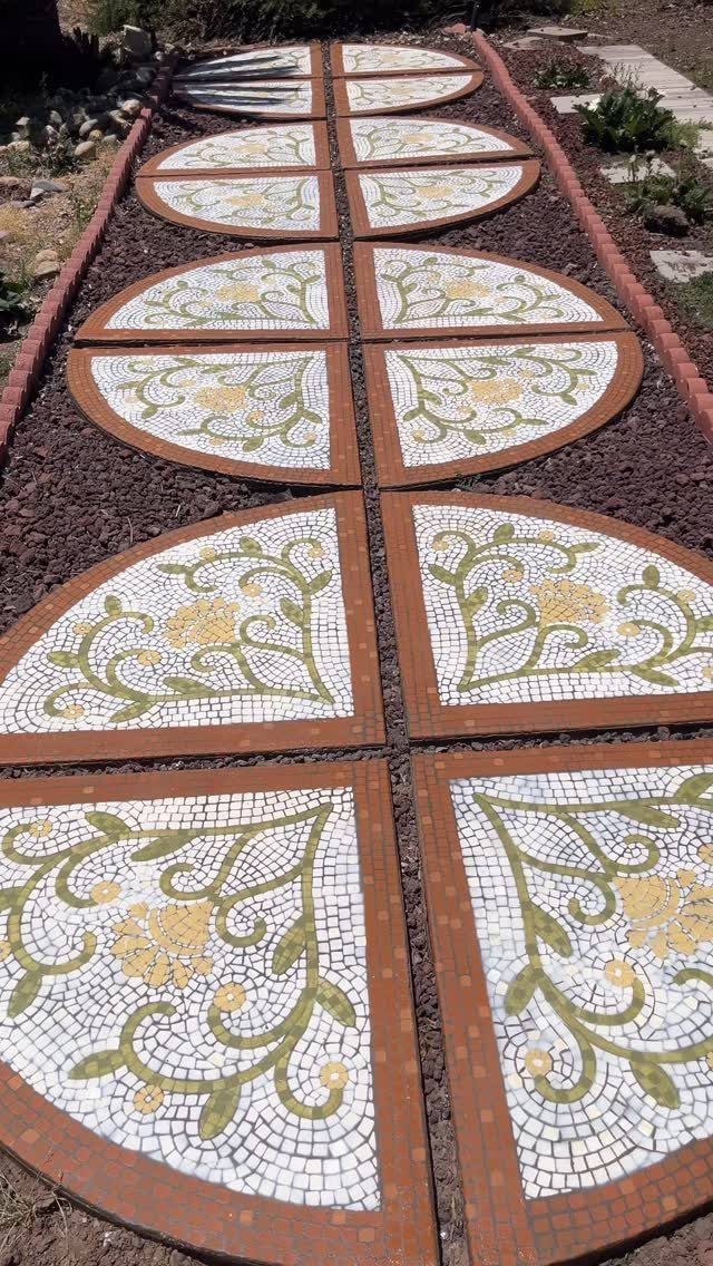 Circular mosaic stepping stones with floral patterns laid in a row along a garden path.