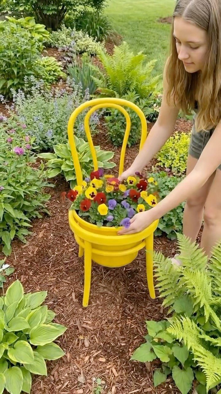 A girl placing colorful pansies into a bright yellow vintage chair used as a garden planter.