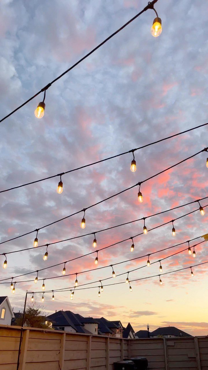 Glowing string lights hang across a backyard under a pink and blue sunset sky.