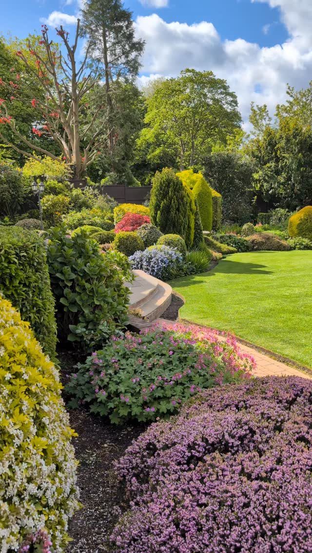 18 Yard Layout Ideas with Photos for Front and Back Spaces 14 Lush garden landscape with colorful flowering perennials, green shrubs, and a manicured lawn under a blue sky.
