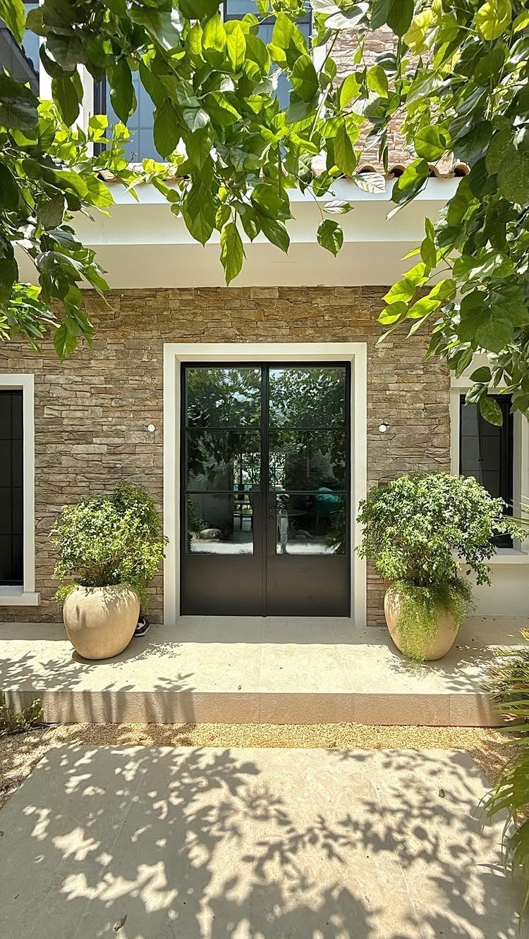 18 Yard Layout Ideas with Photos for Front and Back Spaces 3 Black French doors set in a stone wall flanked by two large potted plants.
